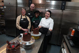 Four chefs posing with chocolate cakes in a kitchen setting