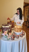 Geanina standing behind a table with various cakes and desserts for a wedding.