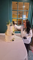 Geanina finishing a wedding cake in front of a window with a teal frame.