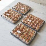 Three clear plastic clamshell containers filled with mini brioche canapes, arranged on a wooden surface outdoors.