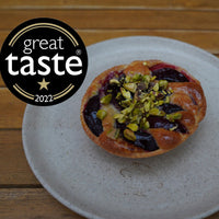 Plum and Pistachios Frangipane tart on a plate, featuring the Great Taste 2022 logo.