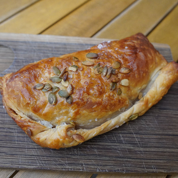 A pastie with a flaky, buttery shortcrust pastry topped with roasted butternut squash, onion, and goat cheese, garnished with pumpkin seeds.