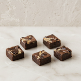 Five brownie squares with cream cheese swirls on a marble surface.