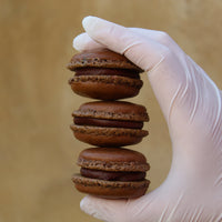 Box of 24 flourless dark chocolate macarons with crisp almond shells and rich ganache, handcrafted in North London patisserie