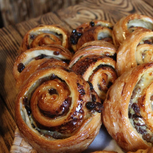 Four handmade Pain au Raisins pastries filled with vanilla custard and golden raisins, glazed and golden, made with 100% butter in North London